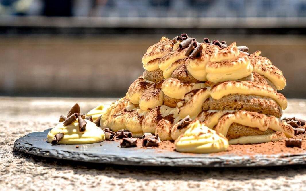 Tiramisù sul piatto d'ardesia appoggiato sulla spalletta dell'Arno, con i palazzi di Pisa dietro