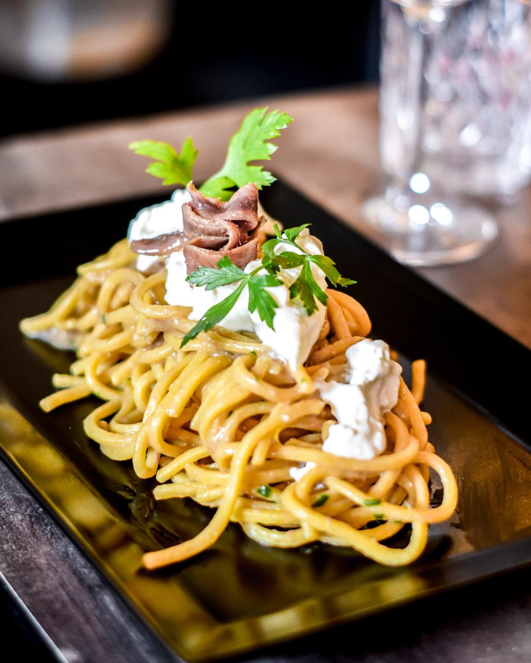 Tonnarelli with stracciatella and anchovies, served on a black plate