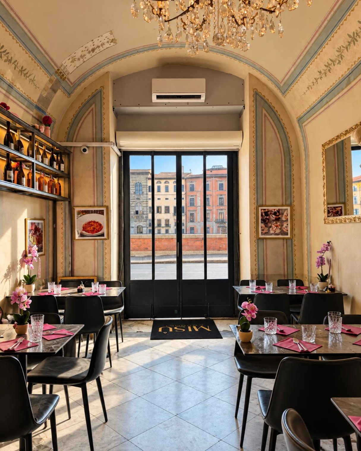The Misù dining room by day: frescoed vault, crystal chandelier, tables with pink napkins and, through the glass door, the riverside palaces