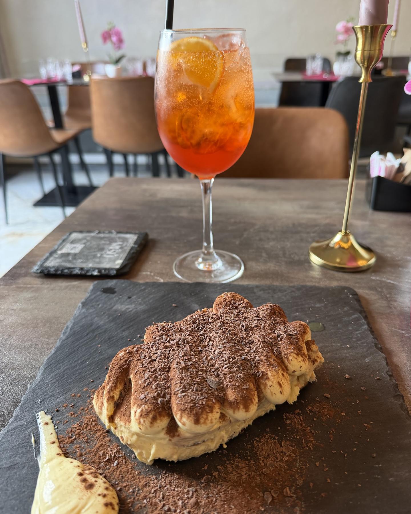 Classic tiramisù dusted with cocoa next to an Aperol spritz, on the wooden table