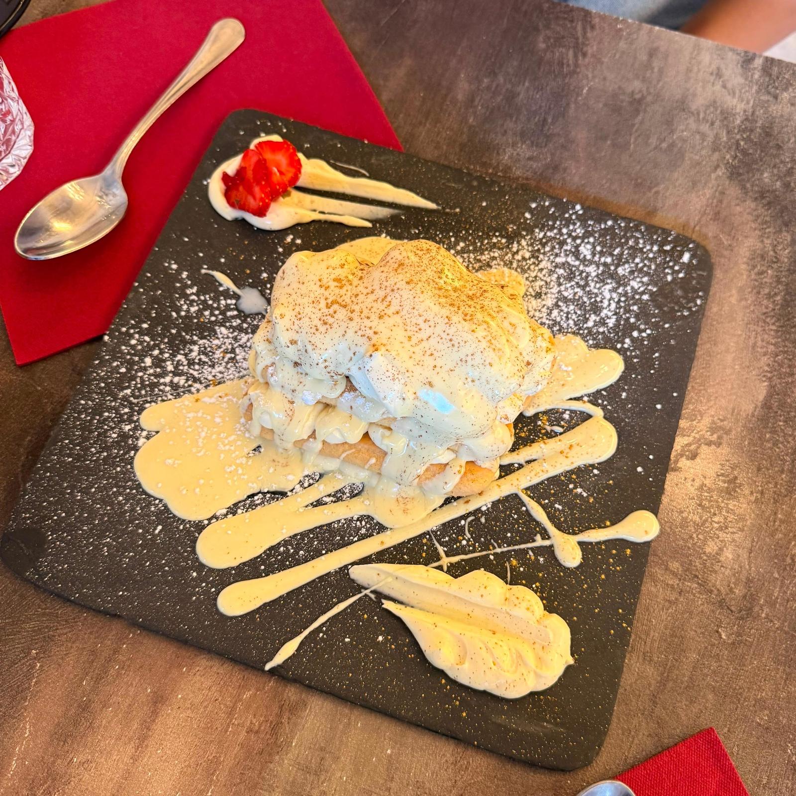 Tiramisù with cream drizzled in stripes on a square slate plate